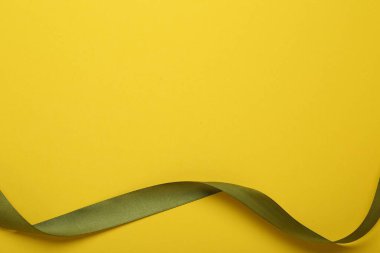 Beautiful green ribbon on yellow background, top view. Space for text