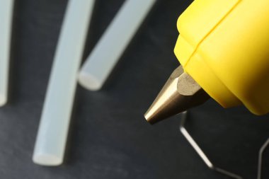 Hot glue gun and sticks on dark grey table, closeup