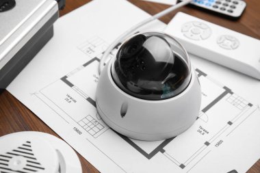 CCTV camera and building plan on wooden table, closeup. Home security system