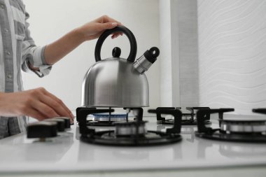 Woman putting kettle on gas stove in kitchen, closeup