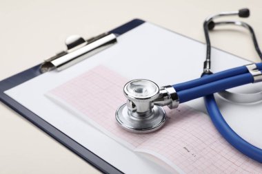 Stethoscope, clipboard and cardiogram paper on beige background, closeup