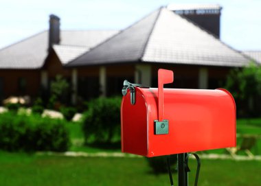 Red letter box and blurred view of modern house with beautiful garden on sunny day