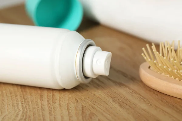 Bottle of dry shampoo and hairbrush on wooden table, closeup