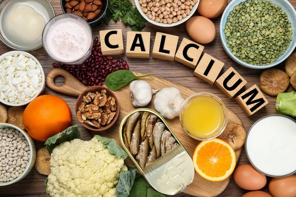 Set of natural food and cubes with word Calcium on wooden table, flat lay