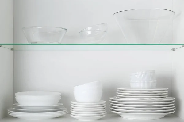 Different clean plates and bowls on shelves in cabinet