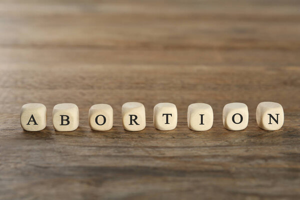 Word Abortion made of cubes on wooden table, closeup