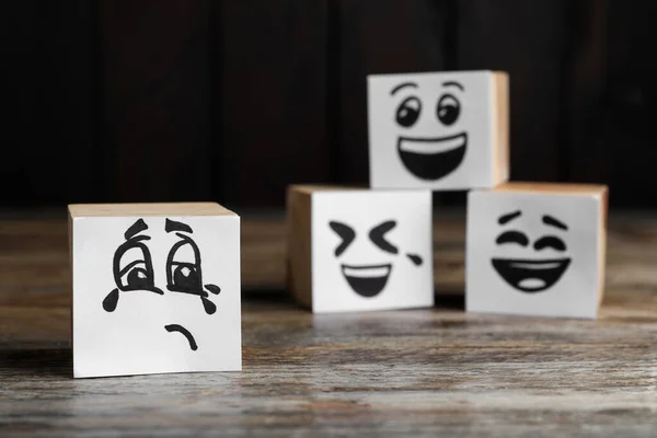 Cubes with sad and funny faces on wooden table. Bullying concept