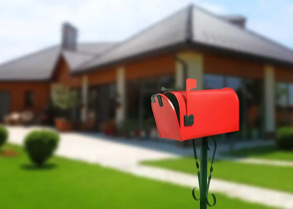 Red letter box and blurred view of modern house with beautiful garden on sunny day, space for text