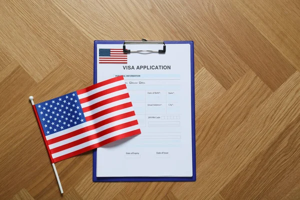 Visa application form for immigration and small American flag on table, flat lay