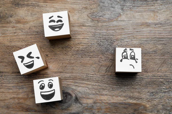 Cubes with sad and funny faces on wooden table, flat lay. Bullying concept