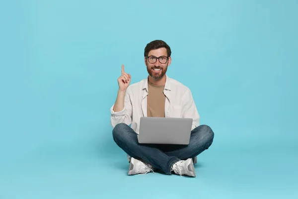 Happy handsome man with laptop sitting on light blue background