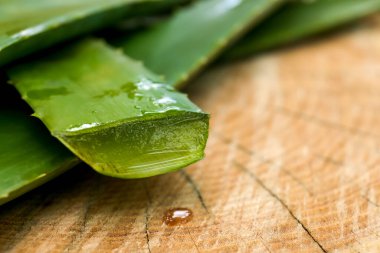 Fresh cut aloe vera leaves with dripping juice on wooden stump, closeup. Space for text