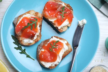 Krem peynirli lezzetli sandviçler, somon balığı ve roka beyaz ahşap masada servis edilir.