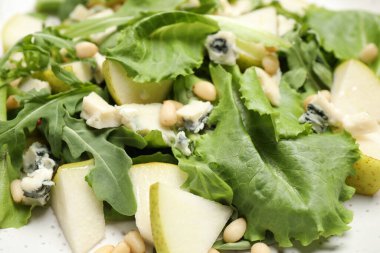 Tasty salad with pear slices, lettuce and pine nuts as background, closeup