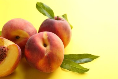 Fresh ripe peaches and green leaves on yellow background, closeup. Space for text