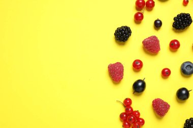 Mix of fresh berries on yellow background, flat lay. Space for text