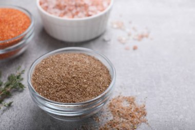 Different kinds of salt on grey table, space for text
