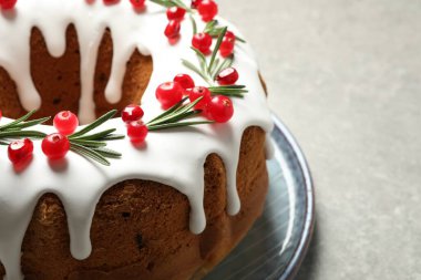 Traditional Christmas cake decorated with glaze, pomegranate seeds, cranberries and rosemary on light grey table, closeup