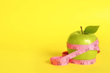 Fresh green apple with measuring tape on yellow background. Space for text