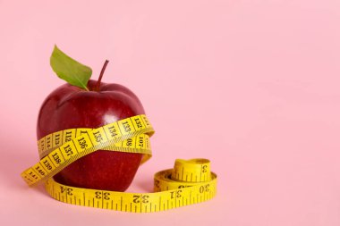 Fresh red apple with measuring tape on pink background. Space for text