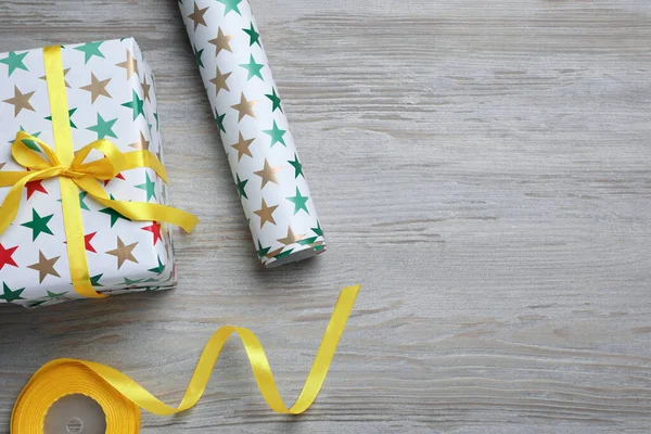 Gift box, wrapping paper roll and yellow ribbon on wooden table, flat lay. Space for text