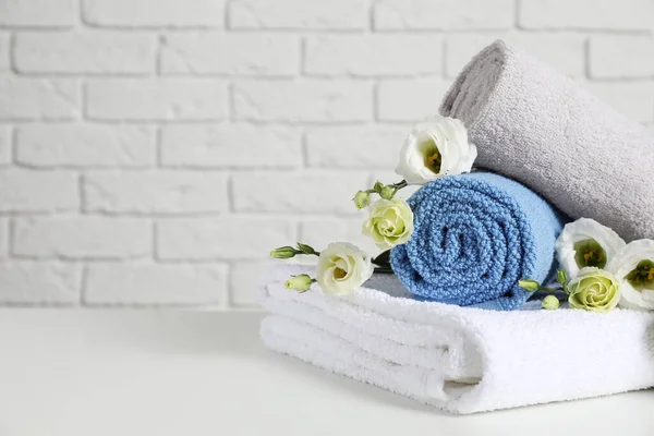 Clean soft towels with flowers on table near white brick wall. Space for text