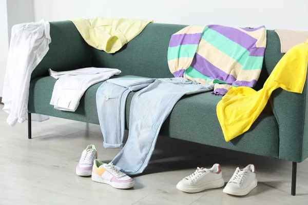 Messy pile of clothes on sofa and shoes in living room