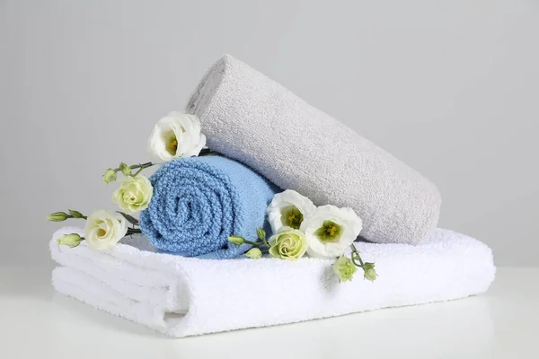 Clean soft towels with flowers on white table against light grey background