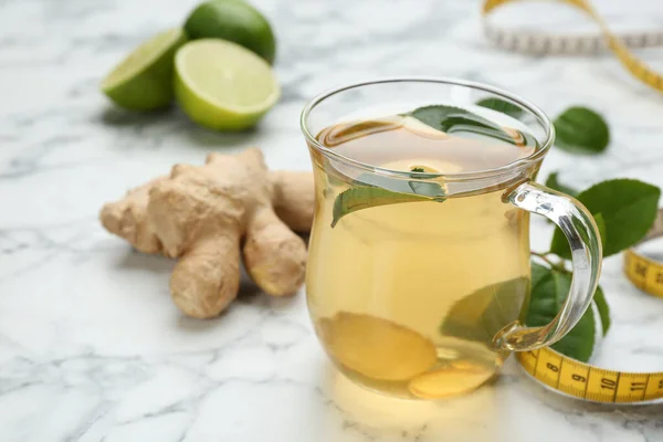 Diet herbal tea with green leaves and ginger on white marble table