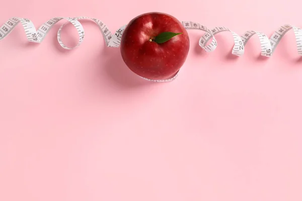 Fresh red apple with measuring tape on pink background, flat lay. Space for text