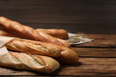 Fresh tasty baguettes and spikelets on wooden table. Space for text