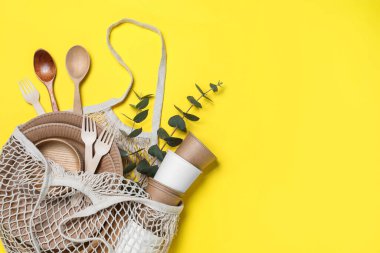 Net bag with different eco items on yellow background, top view and space for text. Recycling concept