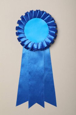 Blue award ribbon on beige background, top view