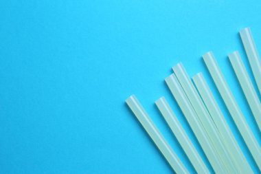 Many glue sticks on light blue background, flat lay. Space for text