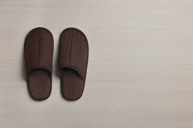 Pair of brown slippers on white wooden floor, top view. Space for text