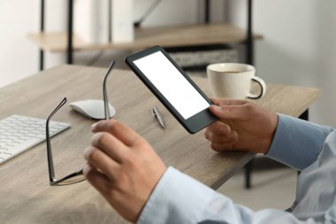 Man using e-book reader at wooden table indoors, closeup