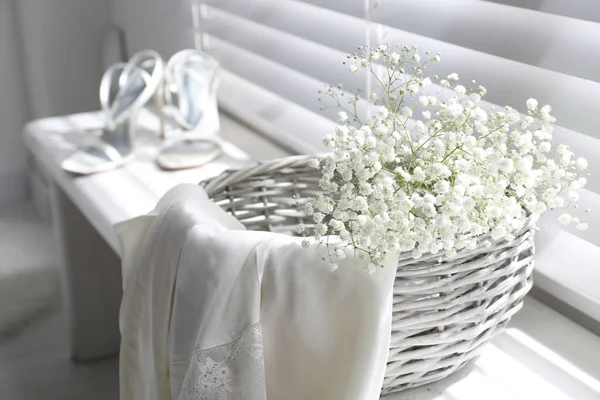 Basket with beautiful flowers and wedding shoes on window sill indoors