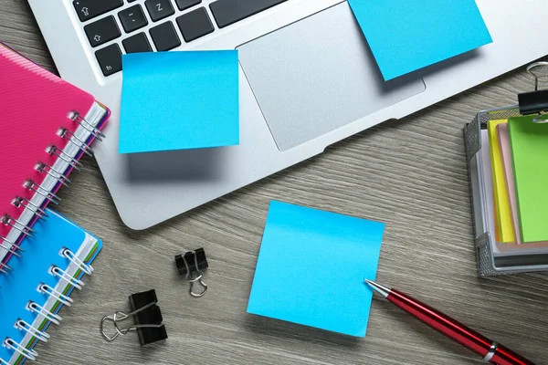 Different sticky notes, laptop and stationery on wooden table, flat lay