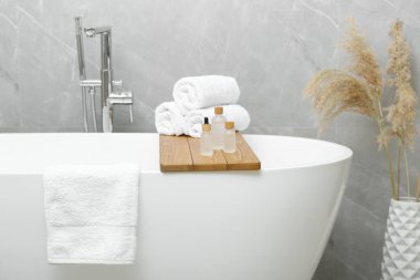 Rolled bath towels and personal care products on tub tray in bathroom