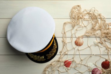 Peaked cap, net and shells on white wooden background, flat lay