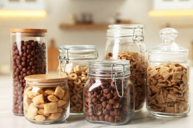 Glass containers with different breakfast cereals on white marble table in kitchen