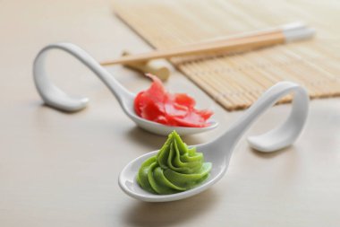 Spoons with swirl of wasabi paste and pickled ginger on white table