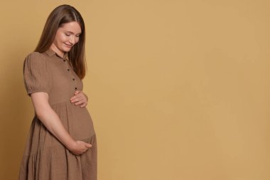 Happy young pregnant woman on light brown background. Space for text
