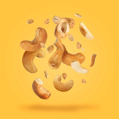 Tasty cashew nuts flying on yellow background