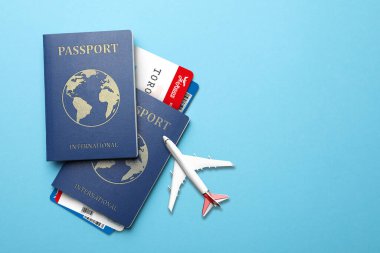 International passports, boarding passes and airplane model on light blue background, flat lay. Space for text