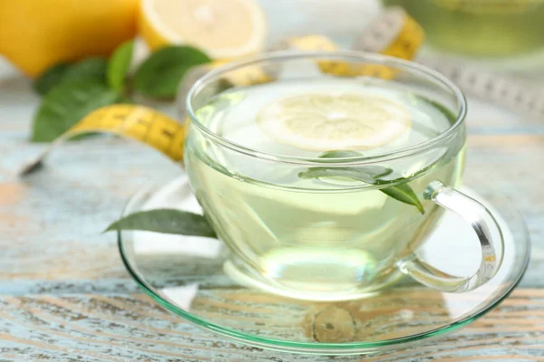 Glass cup of diet herbal tea with green leaves and lemon on wooden table, closeup