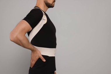 Closeup view of man with orthopedic corset on grey background, space for text