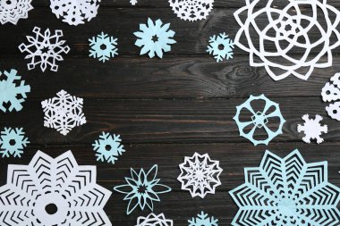 Frame of paper snowflakes on black wooden table, flat lay. Space for text