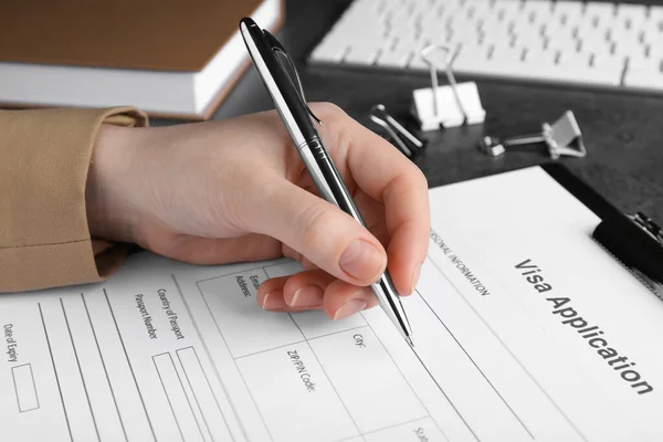 Woman filling visa application form for immigration at grey table, closeup