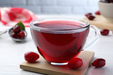 Glass cup of fresh dogwood tea and berries on white wooden table